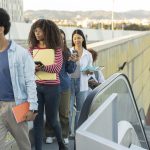 group-diverse-students-are-using-outdoors-escalator-city-are-using-their-smart-phones-as-they-head-their-university
