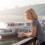 young-blonde-woman-enjoying-city-view-from-bridge-lovely-woman-spending-time-river-embankment-sunset-soft-backlit