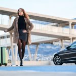 young-business-woman-walking-against-black-luxury-car